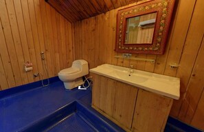 A wooden cabin bathroom with a toilet, sink, and a mirror with a decorative frame.