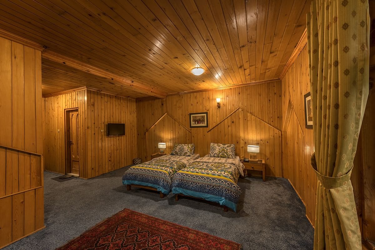Quarto de cabana de madeira com duas camas, um tapete vermelho e uma luminária no teto.