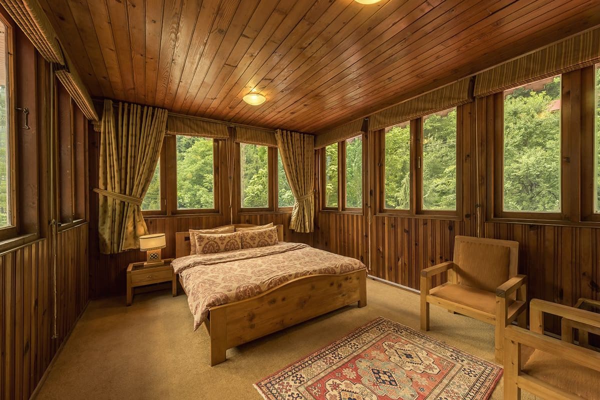 Quarto com painéis de madeira, uma cama grande, uma cadeira e uma mesa de cabeceira.
