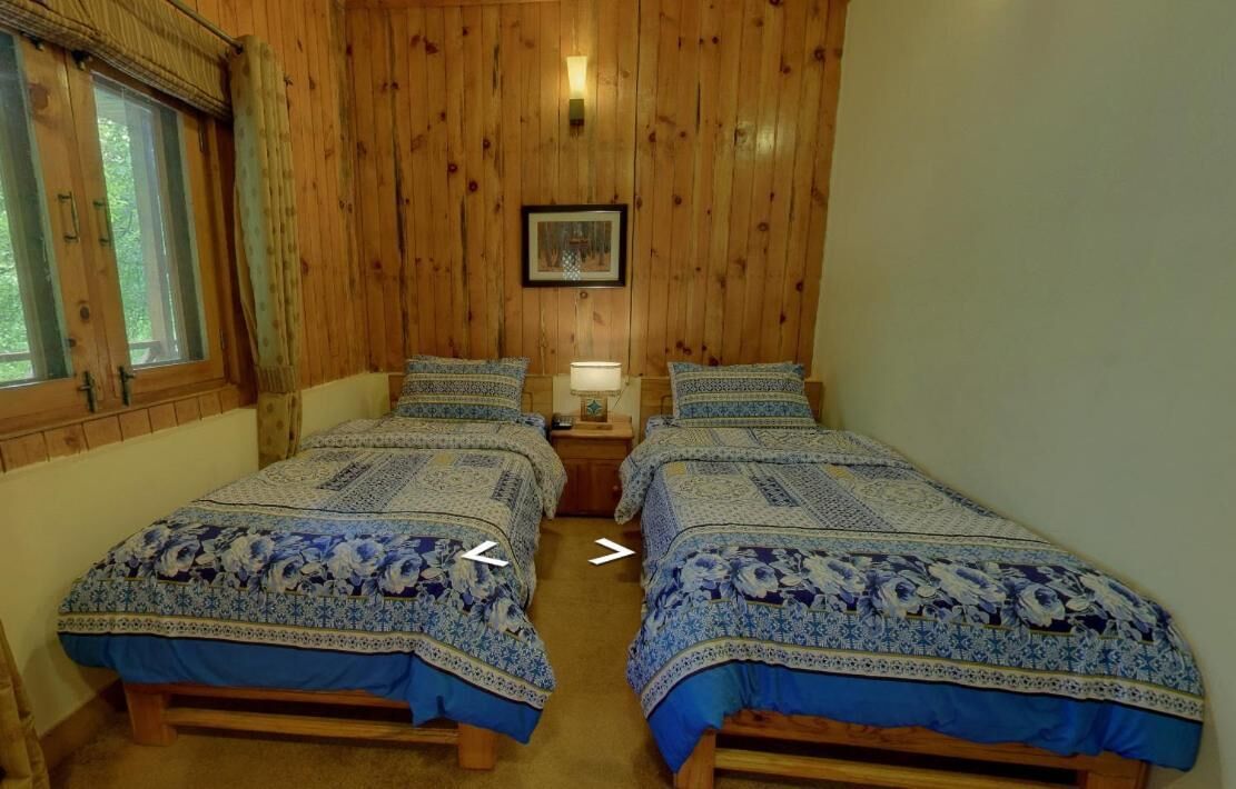 Une chambre avec deux lits en bois, une table de chevet, un tableau encadré au mur et une fenêtre avec des rideaux.