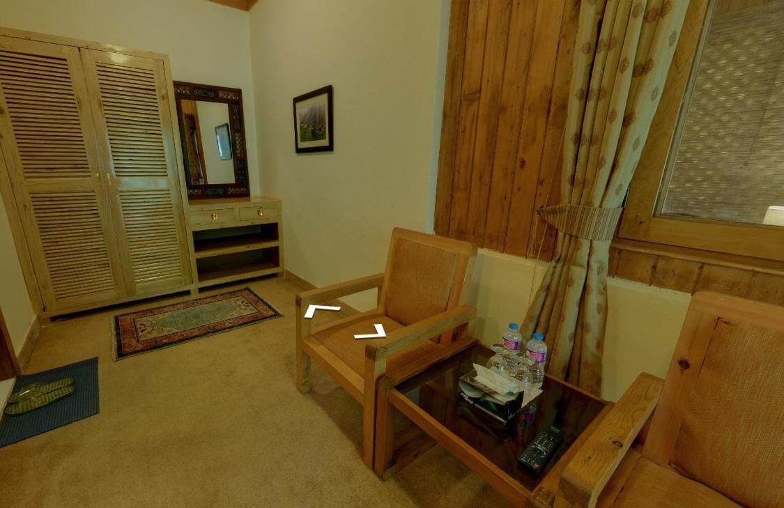 A cozy living room with a wooden chair, a small table with a bottle, and a mirror on the wall.