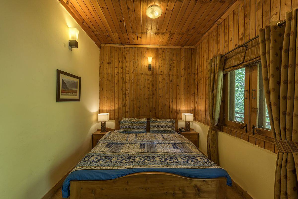 Quarto com painéis de madeira, uma cama, duas luminárias de cabeceira, um quadro na parede e uma janela com cortinas.