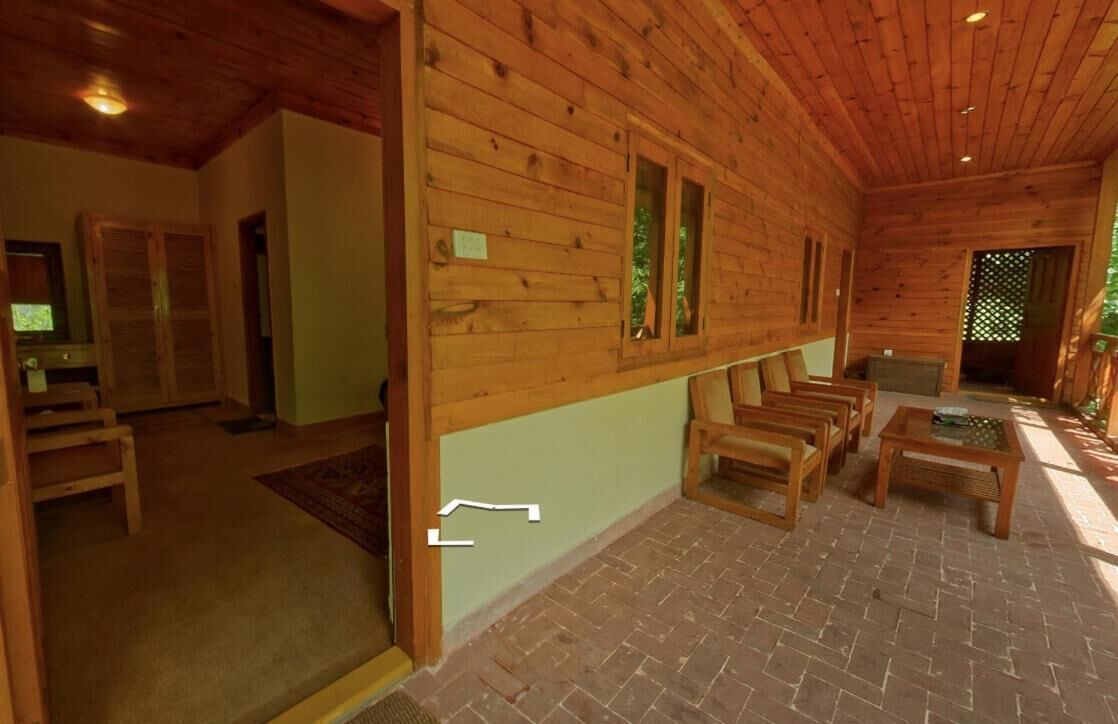 Interno di una baita di legno con pavimento in mattoni, mobili in legno e un piccolo tavolo.