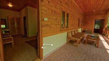 Interior de una cabaña de madera con suelo de ladrillo, mobiliario de madera y una pequeña mesa.