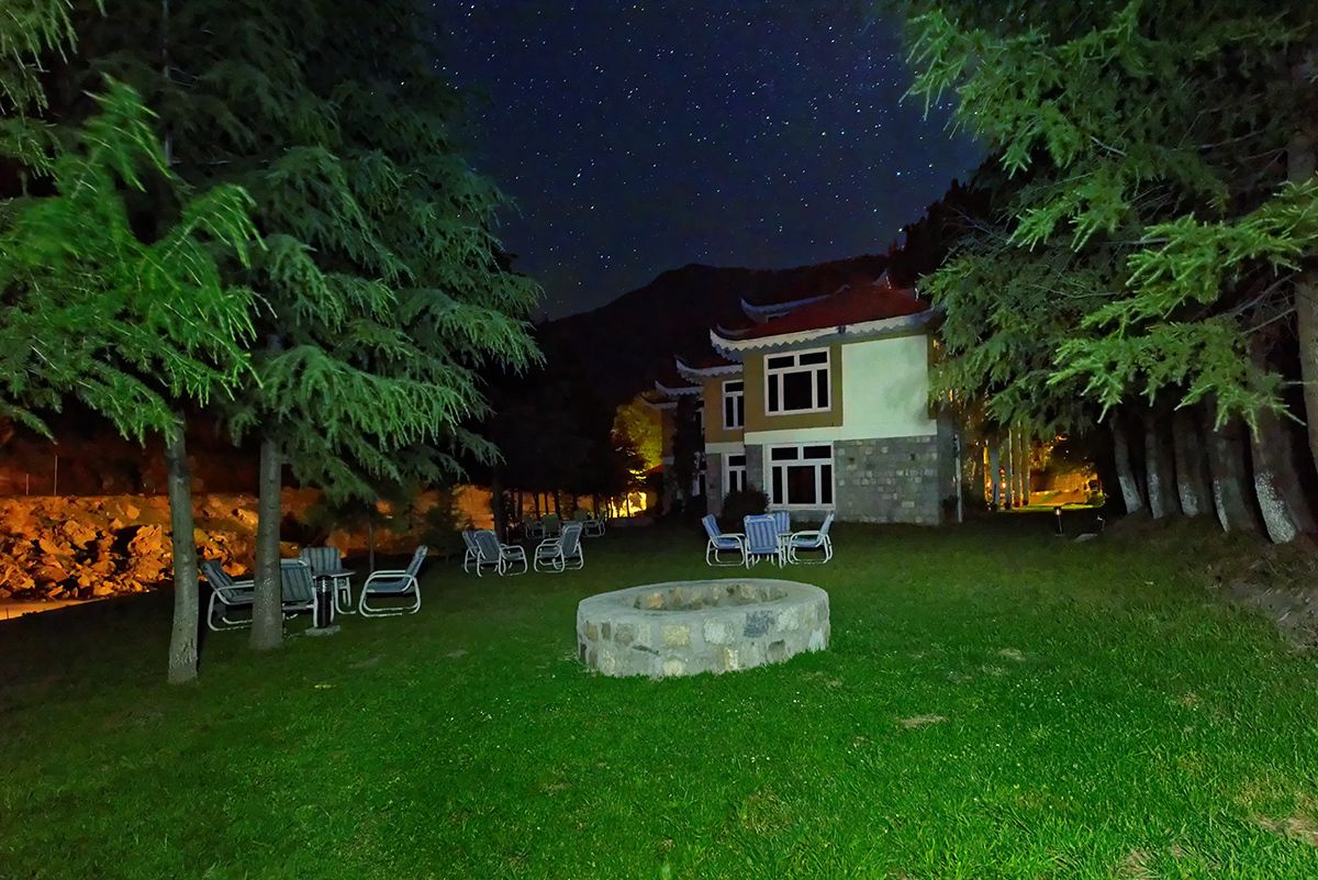 Um pátio com lareira de pedra, espaço para sentar ao ar livre e um edifício com arquitetura tradicional.
