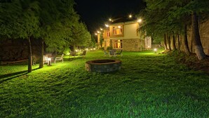 A well-lit outdoor area with a stone fire pit, seating, and a building in the background. - Arcadian Riverside (Balakot)