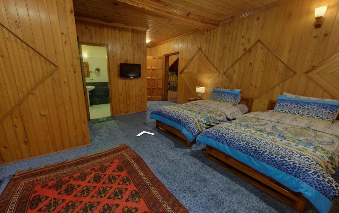 A wooden-paneled room with two beds, a TV, and a bathroom visible through an open door.