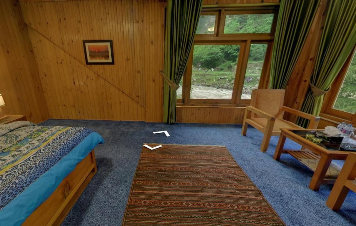A room with a bed, a chair, a small table, and a window with curtains.