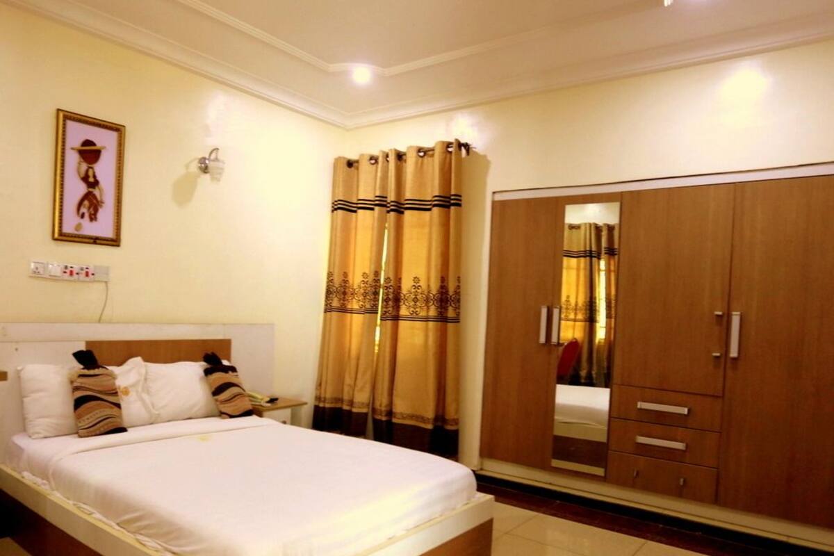 Quarto de hotel com uma cama, cortinas, um guarda-roupa e um candeeiro fixado na parede.