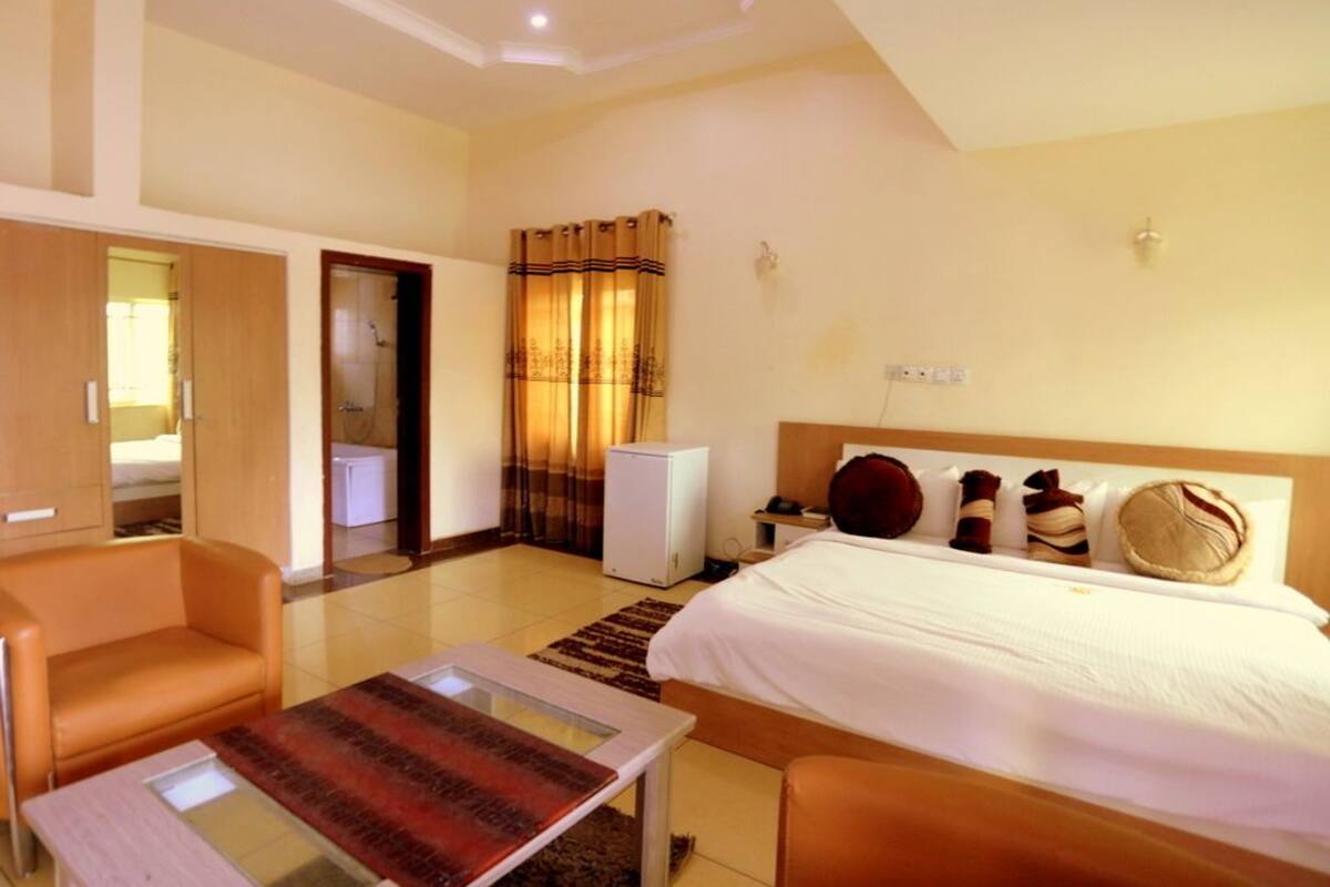 Quarto de hotel com cama, escrivaninha, cadeira, mesa pequena e banheiro visível por uma porta aberta.