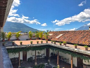 Enjoy panoramic views of the surrounding mountains from this rooftop terrace, featuring a seating area with tables and chairs amidst lush potted plants.