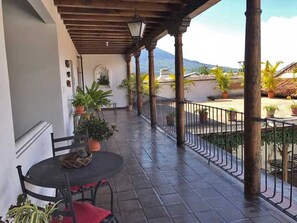 A covered outdoor patio with a table and chairs, potted plants, and a view of the landscape.