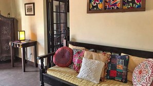 A cozy living room with a wooden sofa, a small side table, and a door leading to another room. - Casita El Balcón (Antigua Guatemala)