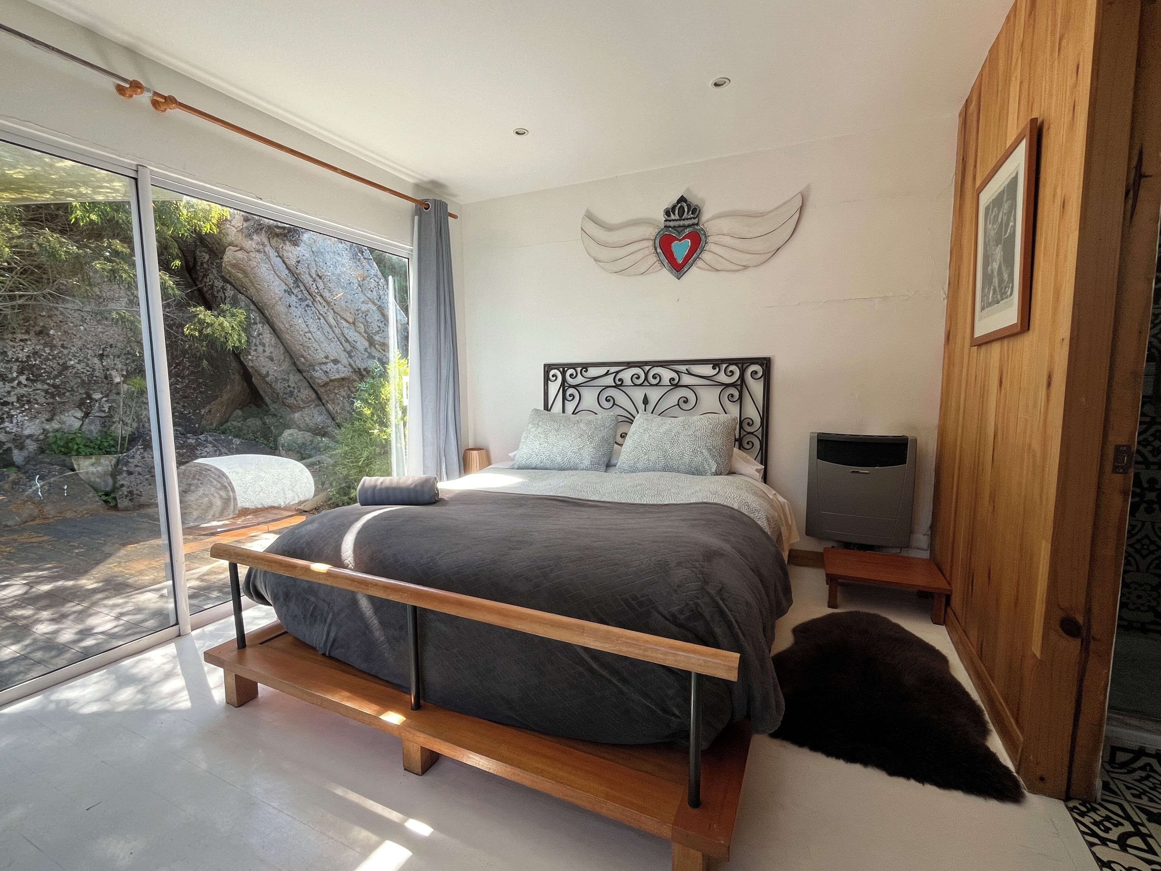 A bedroom with a bed, a TV, a wooden door, and a stone wall.