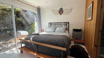 A bedroom with a bed, a TV, a wooden door, and a stone wall.