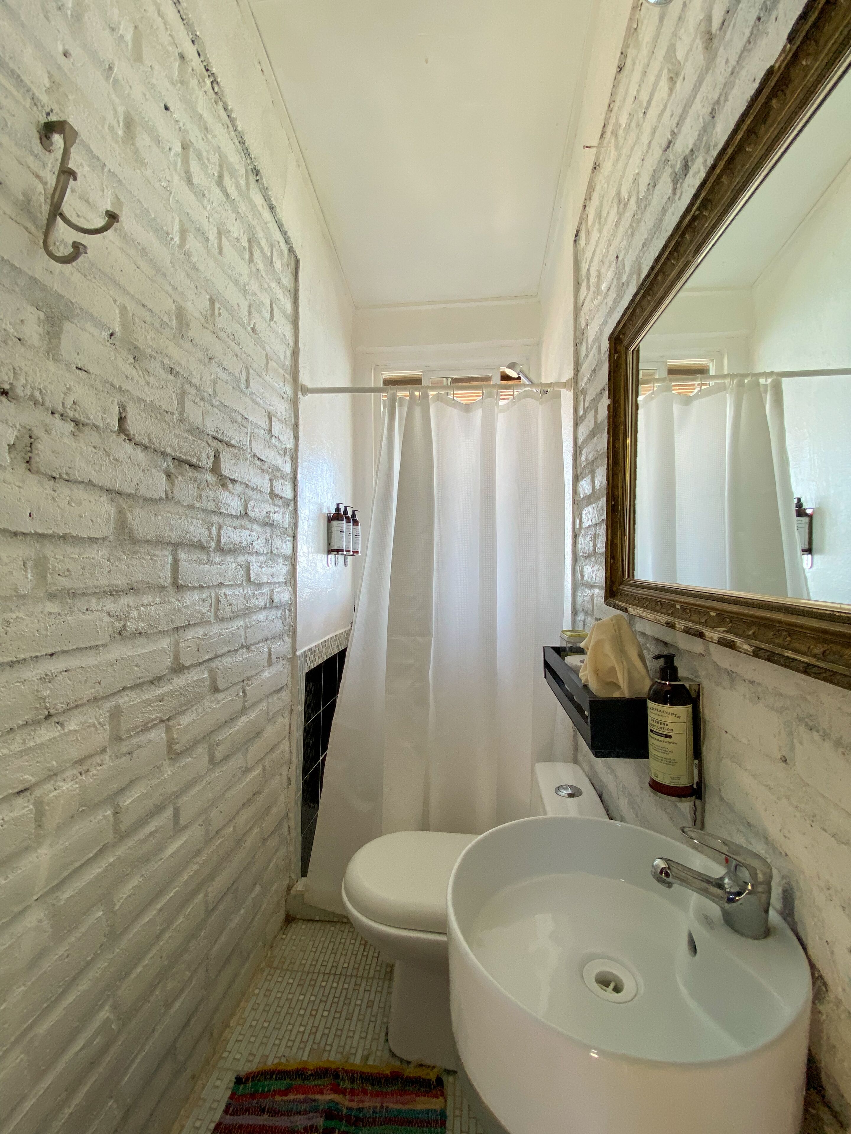 Un baño con lavamanos, inodoro y cortina de ducha blancos. Hay un espejo sobre el lavamanos y una toalla colgada en la pared.