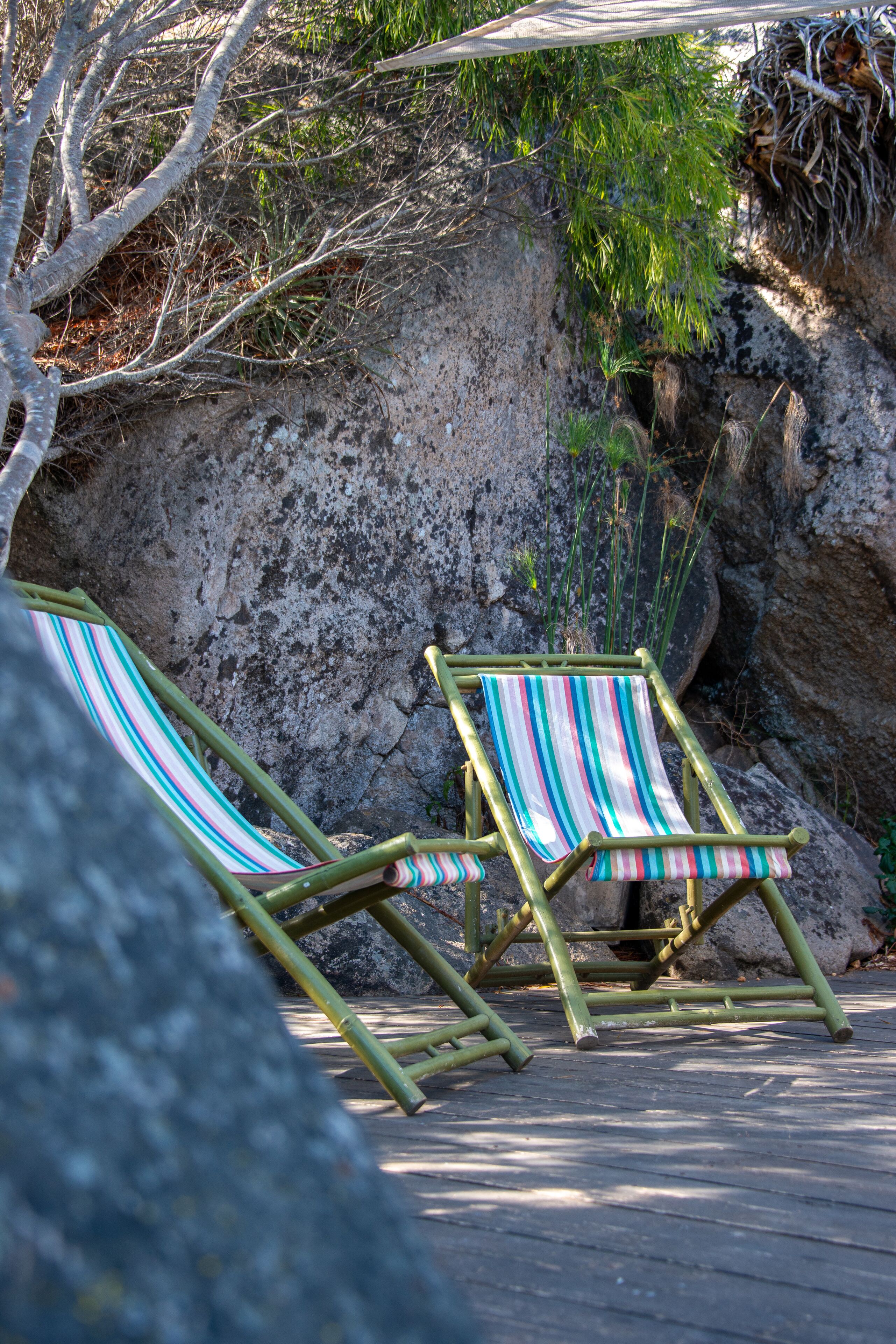 Two striped lounge chairs on a wooden deck with a rocky backdrop.