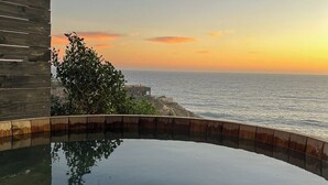 A pool with a wooden deck and a view of the ocean at sunset.