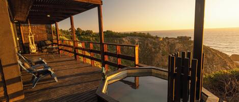 A wooden deck with lounge chairs, a hot tub, and a view of the ocean.