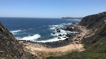 Paesaggio costiero con scogliere rocciose, una spiaggia sabbiosa e una vista limpida sull'oceano.