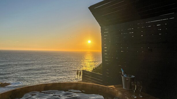 A sunset view from a balcony with a hot tub and a bottle of champagne.