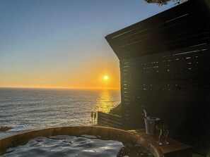 Vista do pôr do sol a partir de uma varanda com hidromassagem e uma garrafa de champanhe.