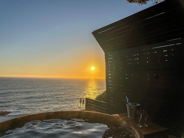 A sunset view from a balcony with a hot tub and a bottle of champagne.