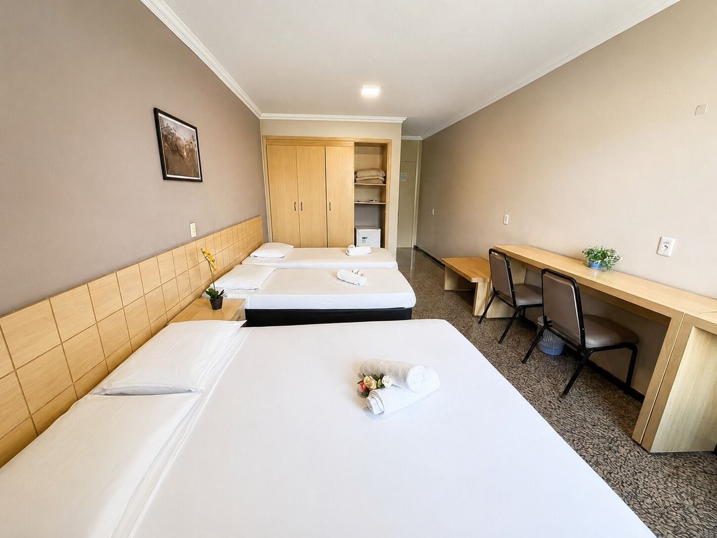Quarto de hotel com duas camas, uma escrivaninha, uma cadeira, uma mesinha e um guarda-roupa.