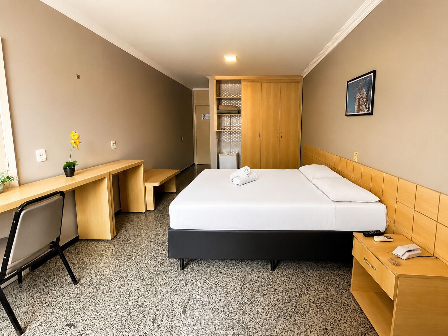 Ein Hotelzimmer mit Bett, Schreibtisch, Stuhl und einem kleinen Tisch mit Pflanze.