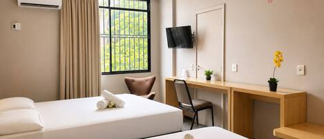 A hotel room with two beds, a desk, a chair, a TV, and a window with a view of greenery.
