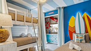 Une chambre avec un lit superposé, une échelle, une commode et des planches de surf accrochées au mur.