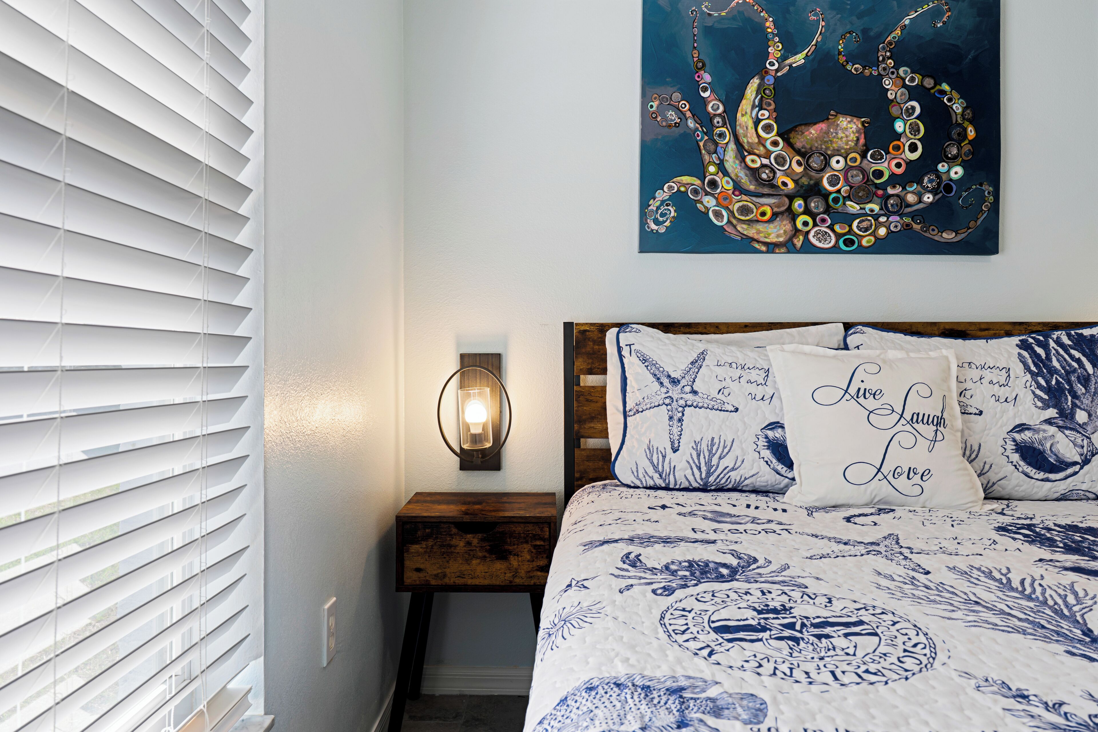Una camera da letto con un letto, una lampada a parete e un'opera d'arte a tema polpo.