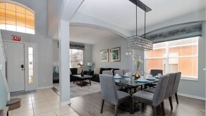 Un comedor amplio con una lámpara moderna, una mesa de comedor preparada para cuatro personas, y vistas al salón contiguo.