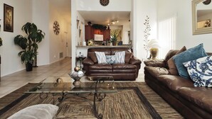 A living room with a glass coffee table, a brown leather sofa, and a patterned rug.