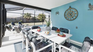 An outdoor dining area with a white table, blue walls, and a large window overlooking a backyard.