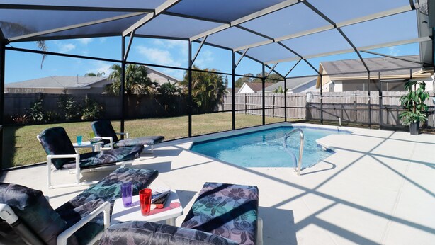 A covered outdoor swimming pool area with lounge chairs and a table.