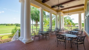 Una veranda coperta con posti a sedere all'aperto, colonne bianche e vista su un campo da golf.