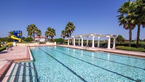 Una piscina con acqua cristallina, uno scivolo acquatico, palme e una zona relax coperta.
