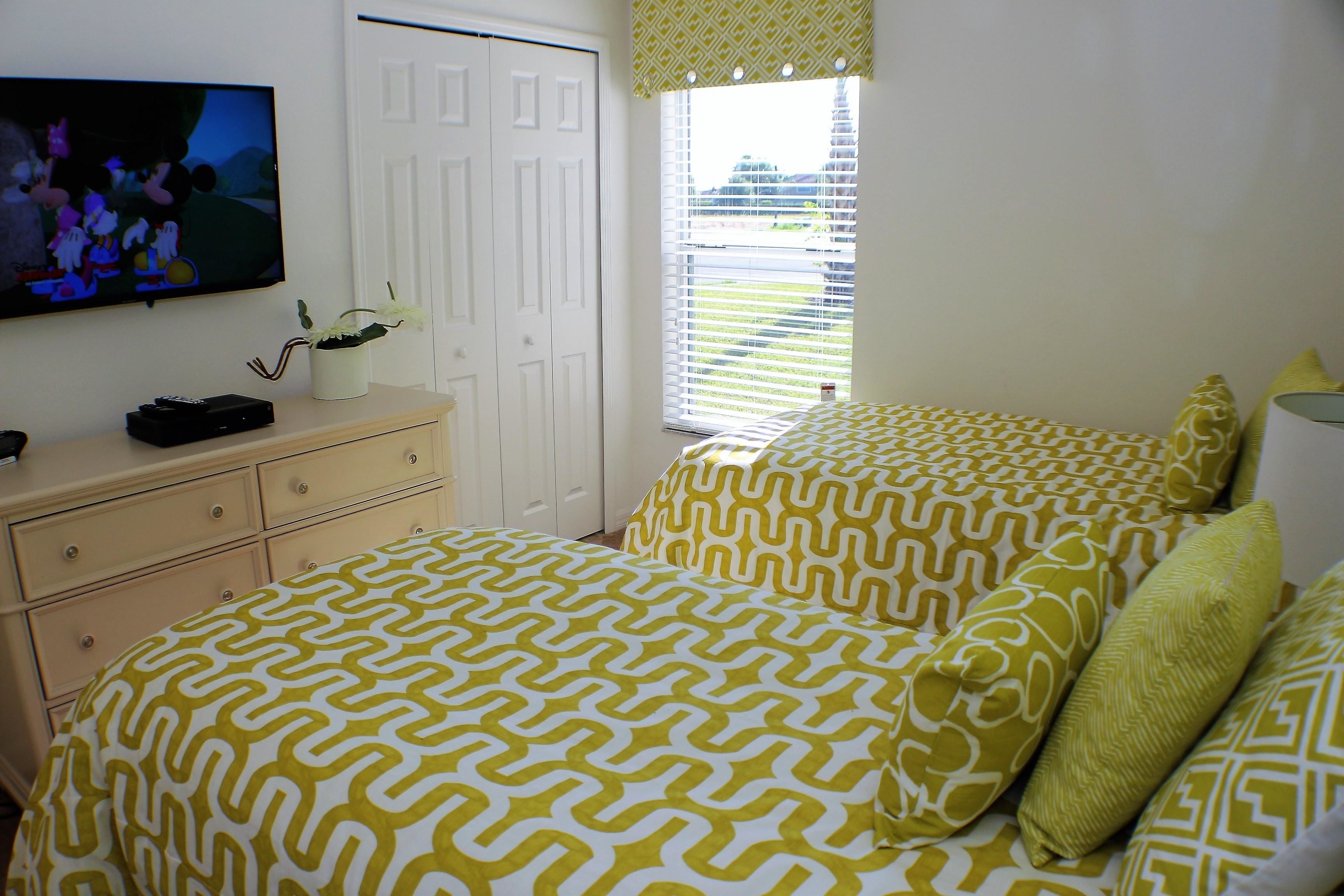 A bedroom with a bed, a dresser, a television, and a window with blinds.