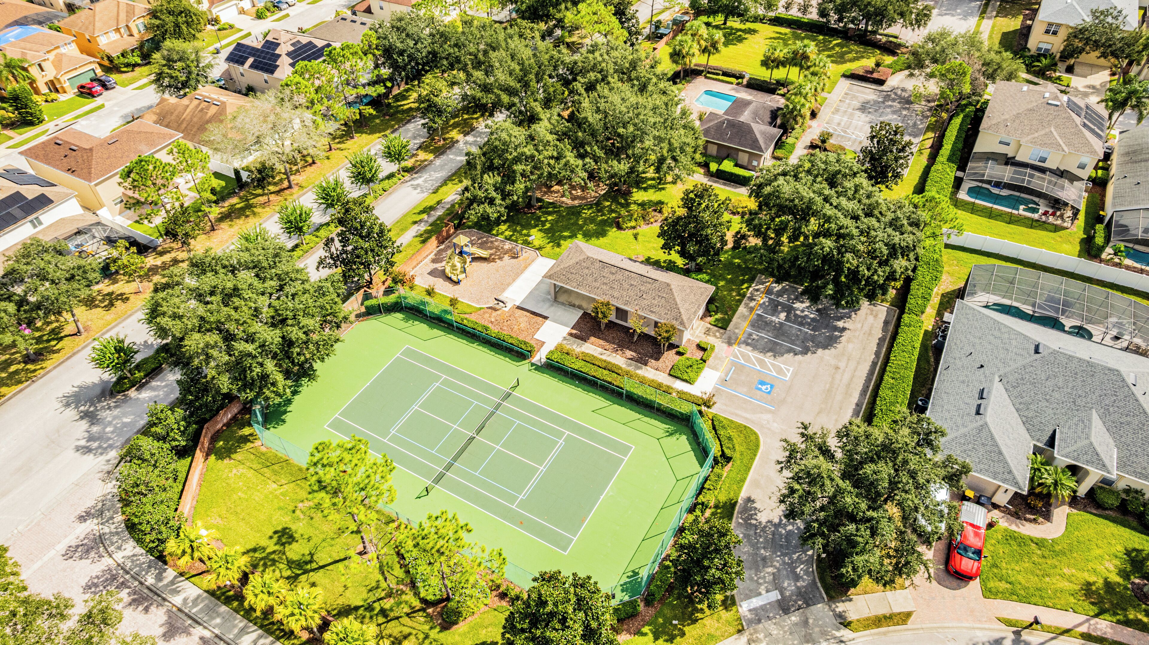 Vue aérienne d’un quartier résidentiel avec un court de tennis, une piscine et plusieurs maisons.