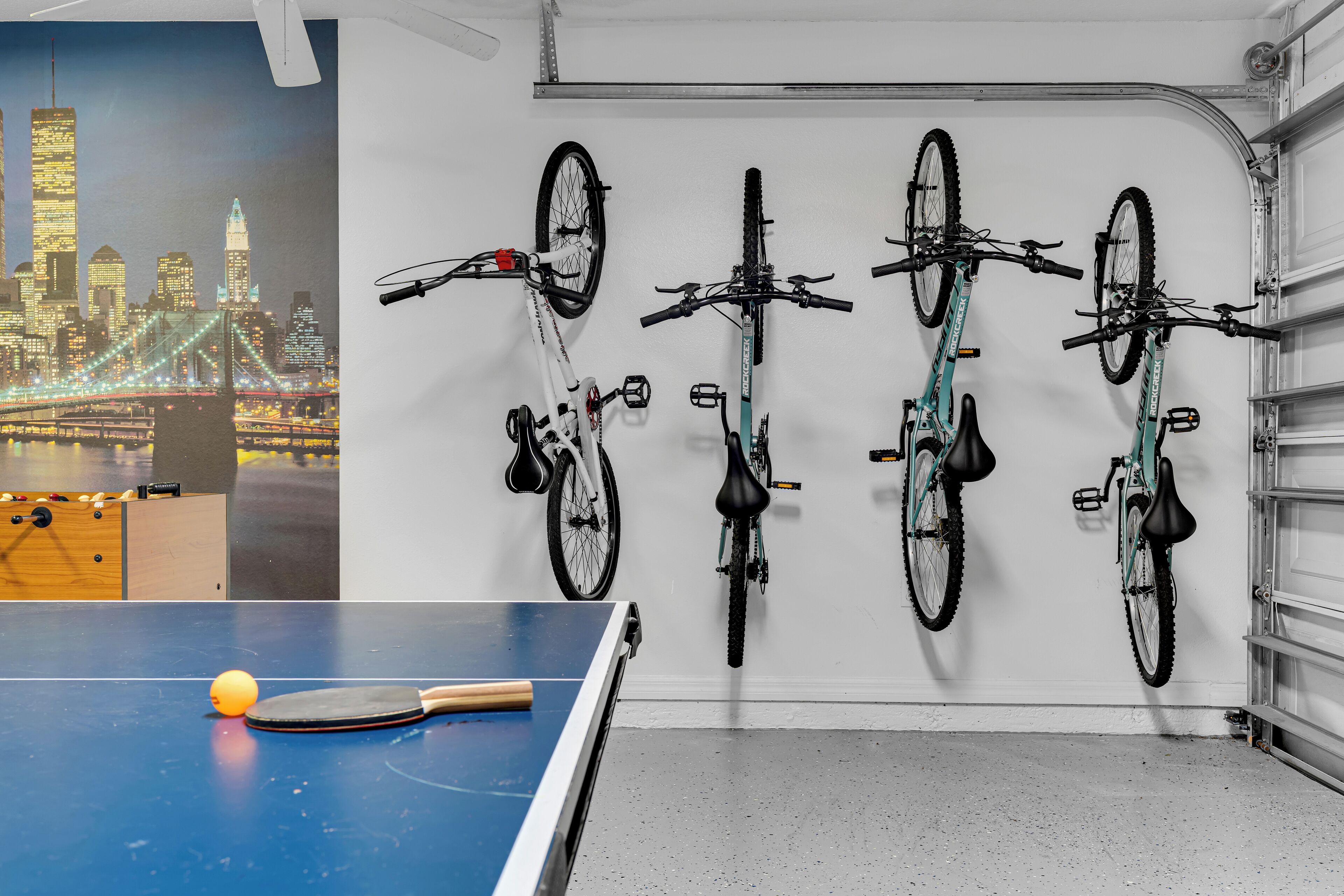 Une pièce avec une table de ping-pong, une fresque représentant un paysage urbain et quatre vélos accrochés au mur.