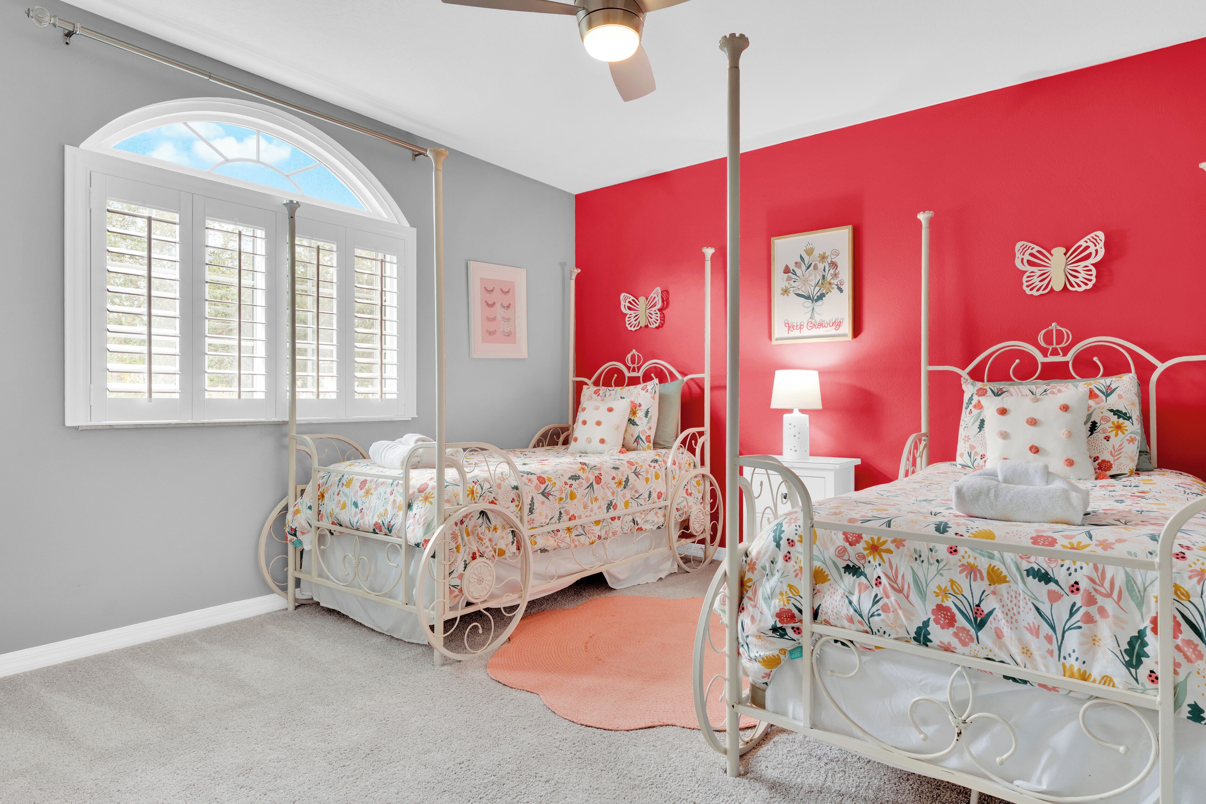 A bedroom with two beds, a window with shutters, a ceiling fan, and butterfly wall decorations.