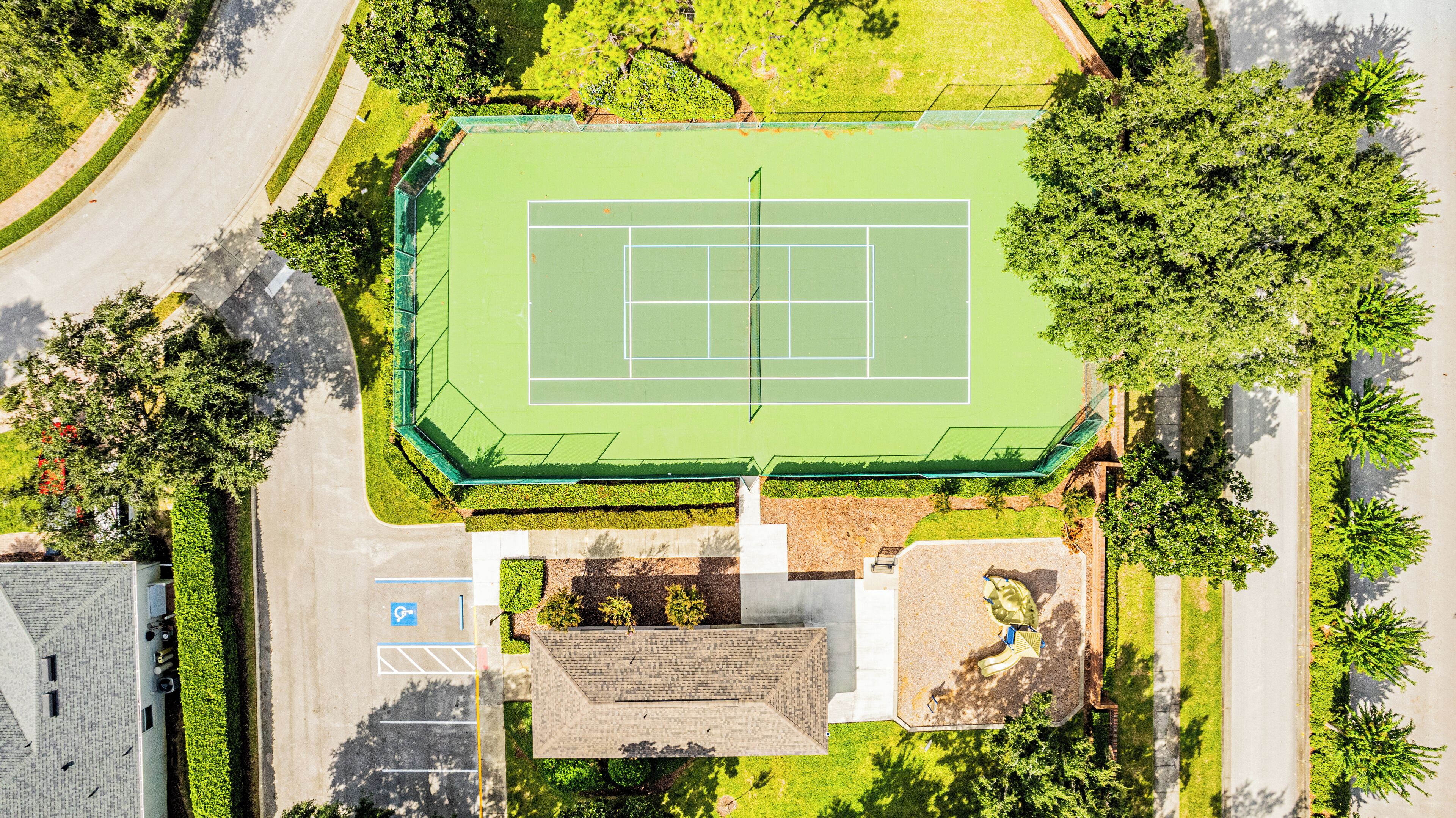 An aerial view of a tennis court surrounded by trees and a parking area.