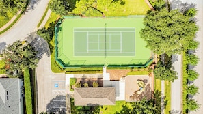 Une vue aérienne d’un court de tennis entouré d’arbres et bordé d’un parking.