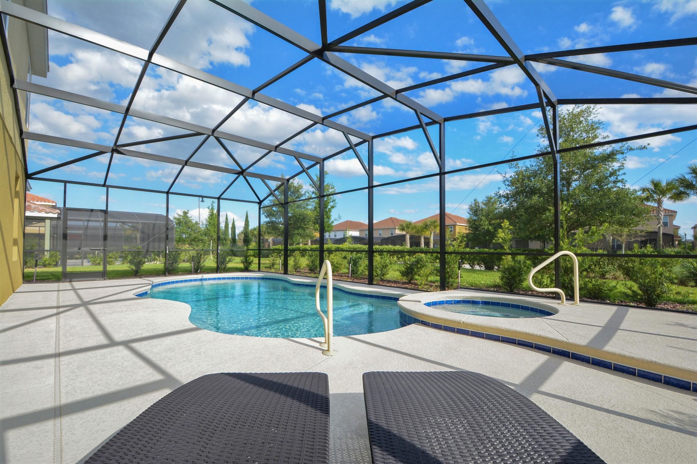 Una piscina interior con agua cristalina y azul, rodeada por un recinto de vidrio y dos sillones de descanso.