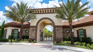 A building entrance with a central archway, palm trees, and a clear blue sky.