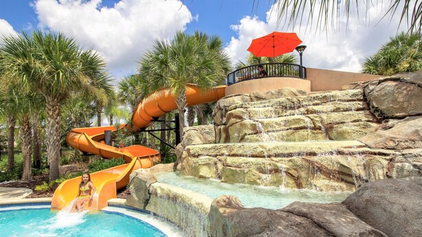 A water park with a pool, a water slide, and a rock formation.
