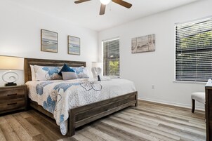 Um quarto com uma cama de madeira, uma mesinha de cabeceira, uma escrivaninha e uma cadeira.