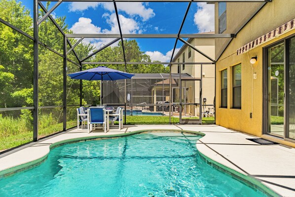 A swimming pool with a covered seating area, a glass-enclosed structure, and a building with large windows.