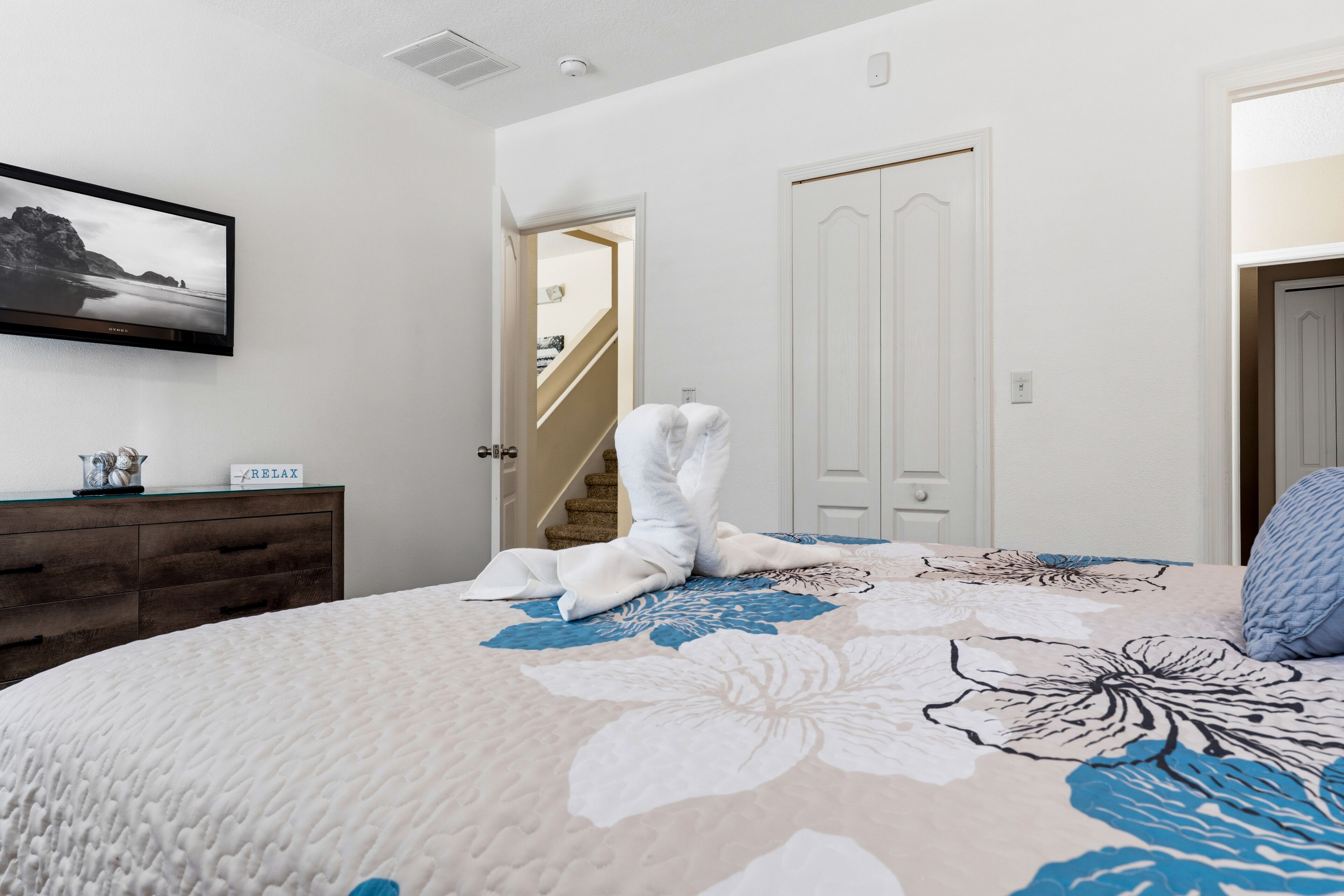 A bedroom with a bed, a dresser, a framed picture, and a staircase leading to another room.
